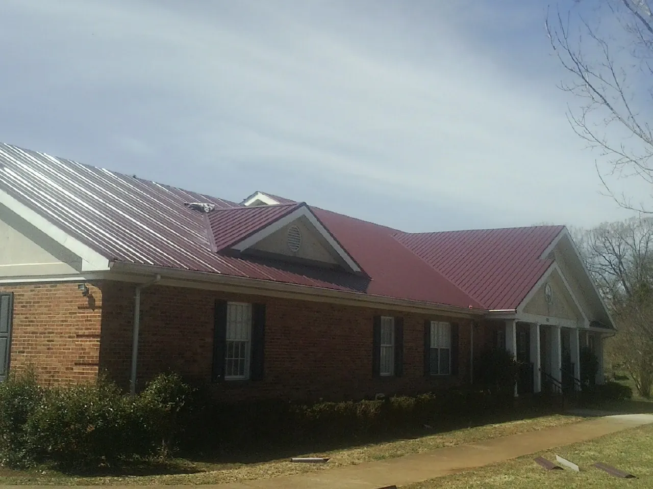 Red metal roof with gabled entries on a long brick building, from a Hail Damage Roof Repair job in Devol