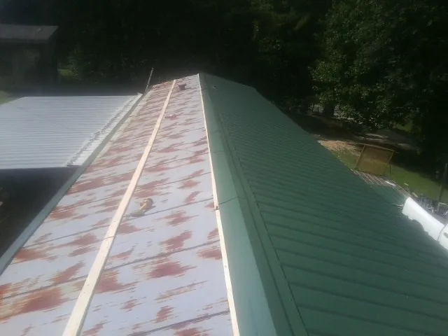 Old rusted panels beside newly installed green metal roofing — Wind Damage Roof Repair by Roofing Brothers in Devol