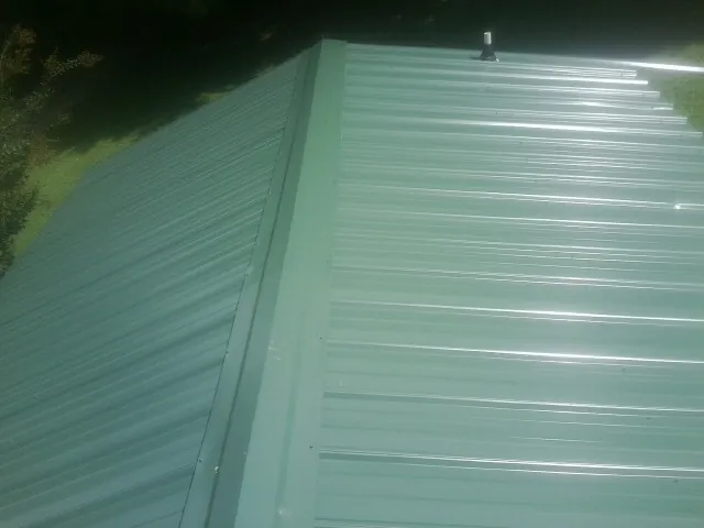 New green metal panels meeting at the ridge of a roof — Flat Roof Repair work by our crew in Devol