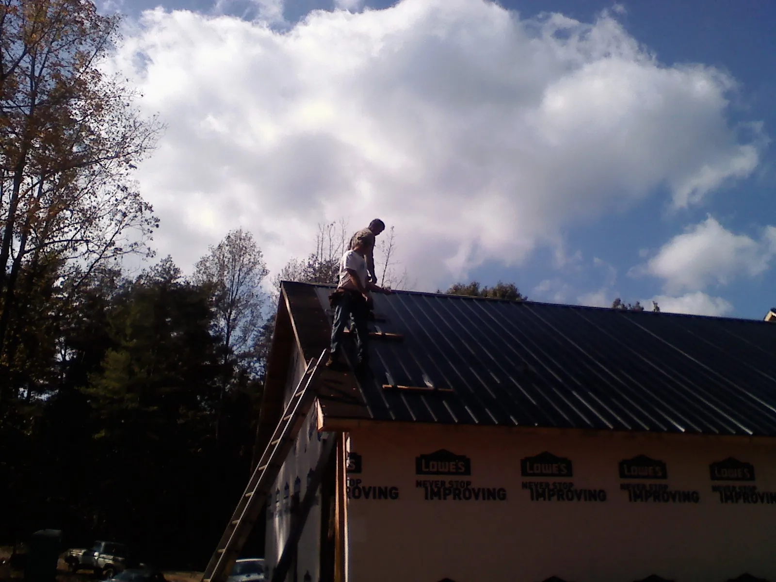 Roofer fastening dark metal panels high against a cloudy sky, from a Roof Inspection job in Devol