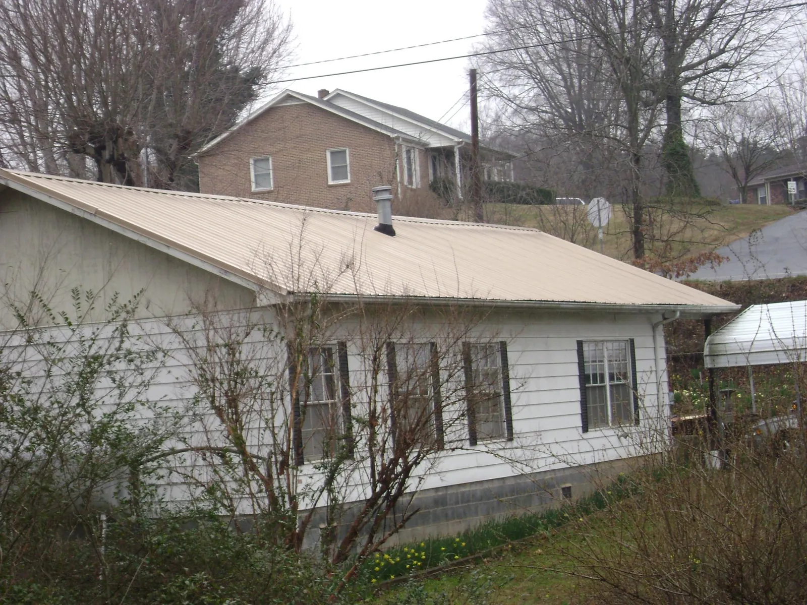 Tan metal roof on a white sided house set into a hillside — Commercial Roofing by Roofing Brothers in Devol