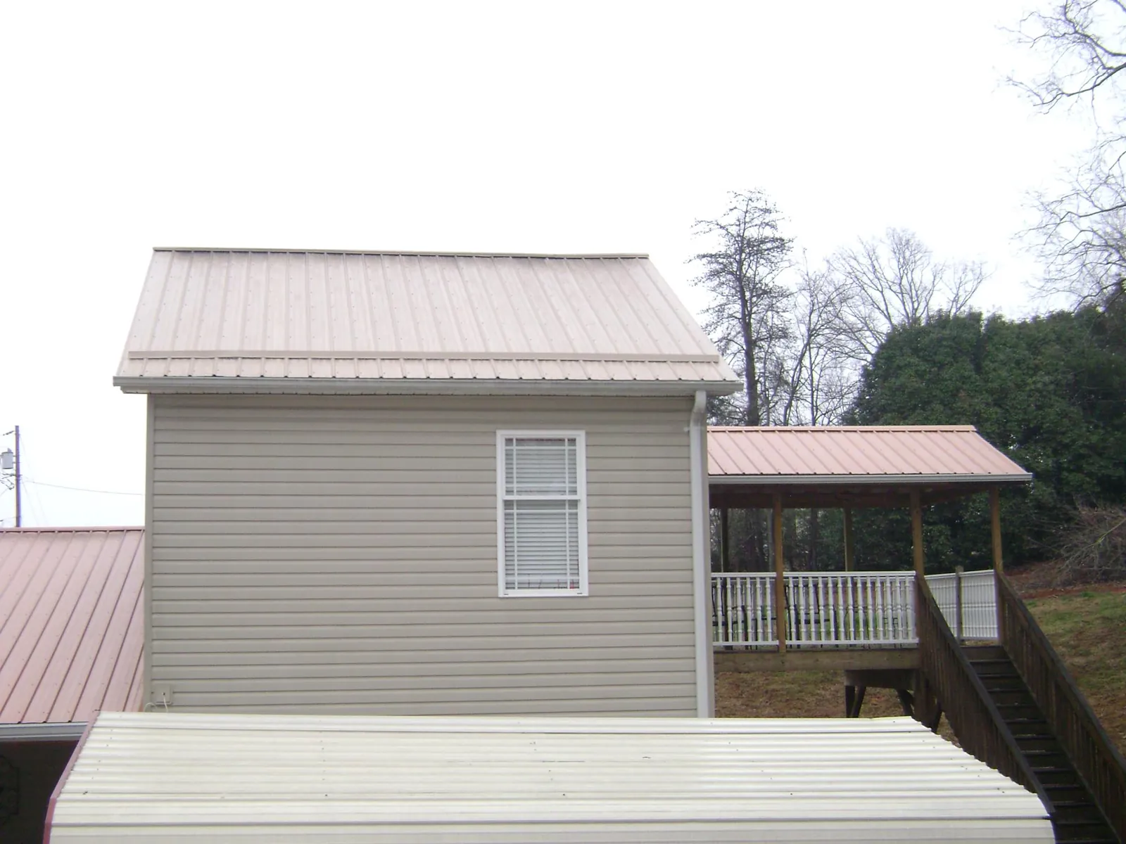 Tan metal roofs on a two story addition and attached porch, from a Roof Replacement job in Devol